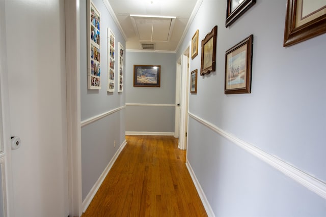 corridor with crown molding, wood finished floors, attic access, baseboards, and visible vents