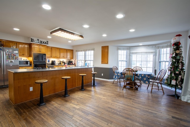 kitchen with dark wood finished floors, a kitchen breakfast bar, and black appliances
