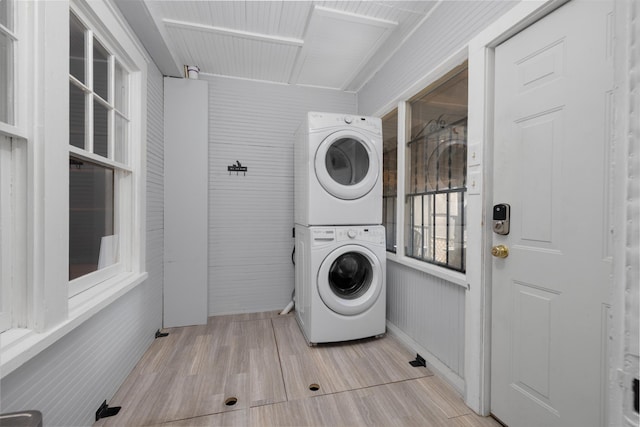 laundry room with wood walls, stacked washing maching and dryer, and light wood-type flooring