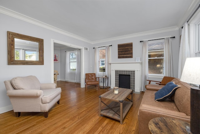 living room featuring a healthy amount of sunlight, a tiled fireplace, crown molding, and light hardwood / wood-style flooring