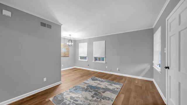 empty room with crown molding, a notable chandelier, and hardwood / wood-style flooring