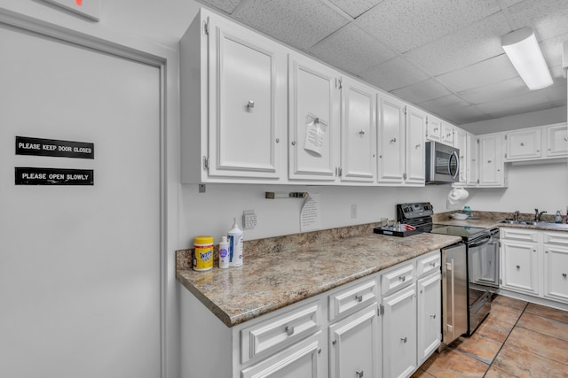 kitchen featuring sink, a drop ceiling, stainless steel appliances, light tile patterned floors, and white cabinets