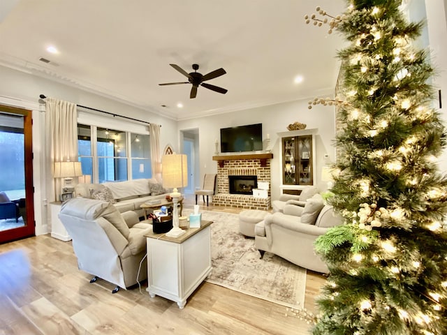 living room with a brick fireplace, ceiling fan, crown molding, and light hardwood / wood-style flooring