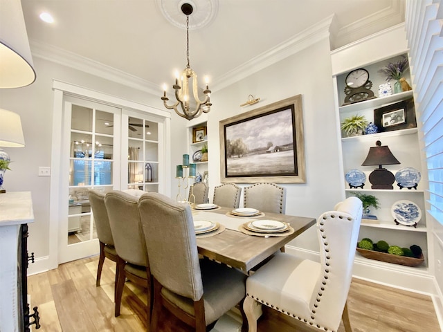 dining space featuring light wood-type flooring, built in features, ornamental molding, and a notable chandelier