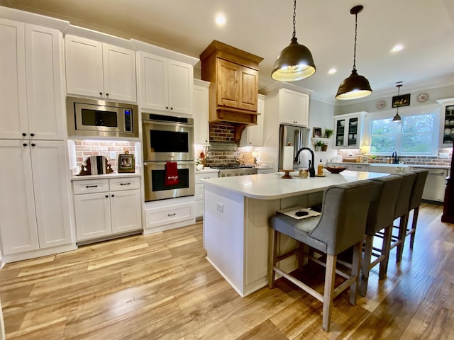 kitchen with backsplash, stainless steel appliances, a kitchen island with sink, white cabinets, and hanging light fixtures