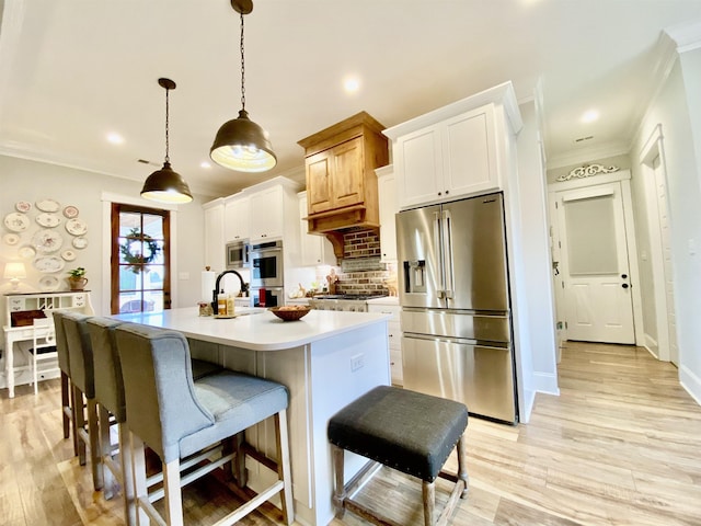 kitchen featuring white cabinets, appliances with stainless steel finishes, hanging light fixtures, and an island with sink