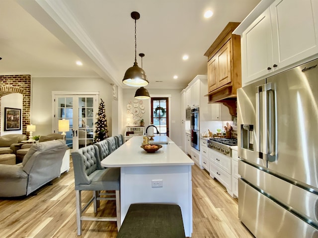 kitchen featuring stainless steel appliances, light hardwood / wood-style flooring, pendant lighting, a kitchen island with sink, and white cabinets