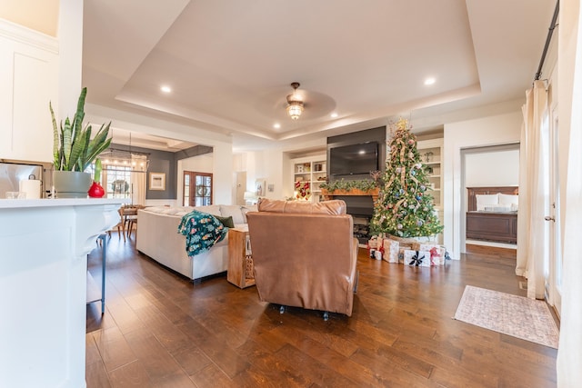 living room featuring built in shelves, dark hardwood / wood-style flooring, a raised ceiling, and a chandelier