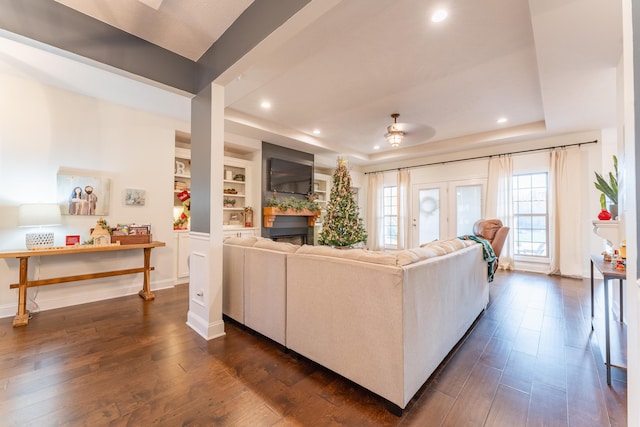 living room featuring built in shelves, ceiling fan, a tray ceiling, and dark hardwood / wood-style flooring