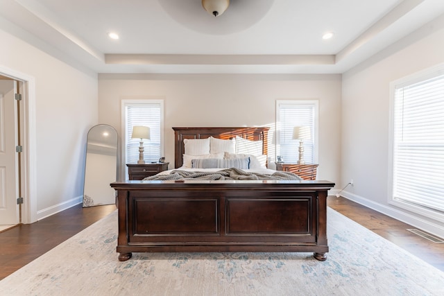 bedroom with a raised ceiling, dark wood-type flooring, and multiple windows