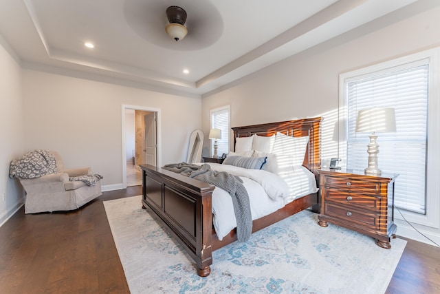 bedroom featuring ceiling fan, a raised ceiling, dark hardwood / wood-style flooring, and multiple windows