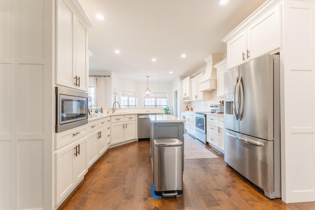 kitchen with appliances with stainless steel finishes, white cabinetry, custom range hood, hanging light fixtures, and decorative backsplash