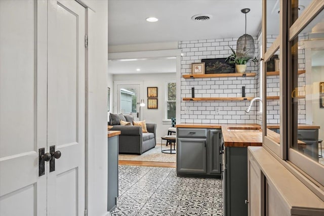 kitchen featuring tasteful backsplash, butcher block countertops, hanging light fixtures, and sink