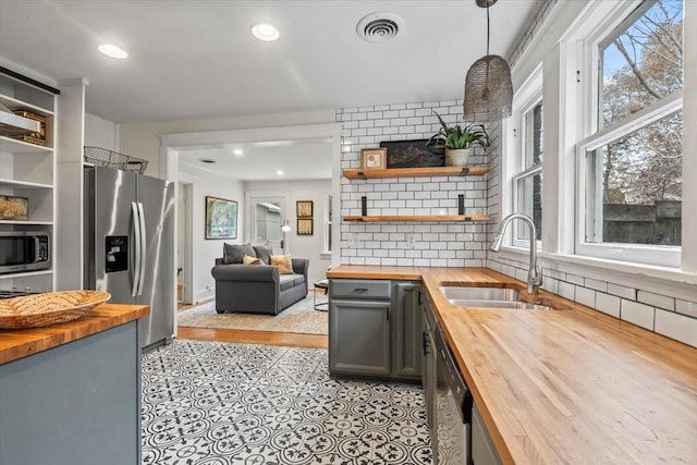 kitchen featuring appliances with stainless steel finishes, hanging light fixtures, butcher block counters, and sink