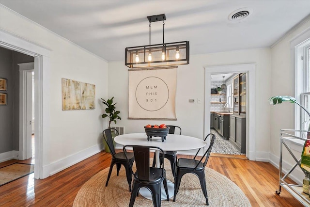 dining room featuring a chandelier, crown molding, sink, and light hardwood / wood-style floors