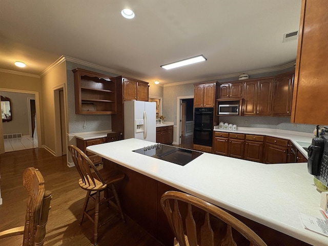 kitchen with dark wood-type flooring, kitchen peninsula, a breakfast bar, black appliances, and ornamental molding