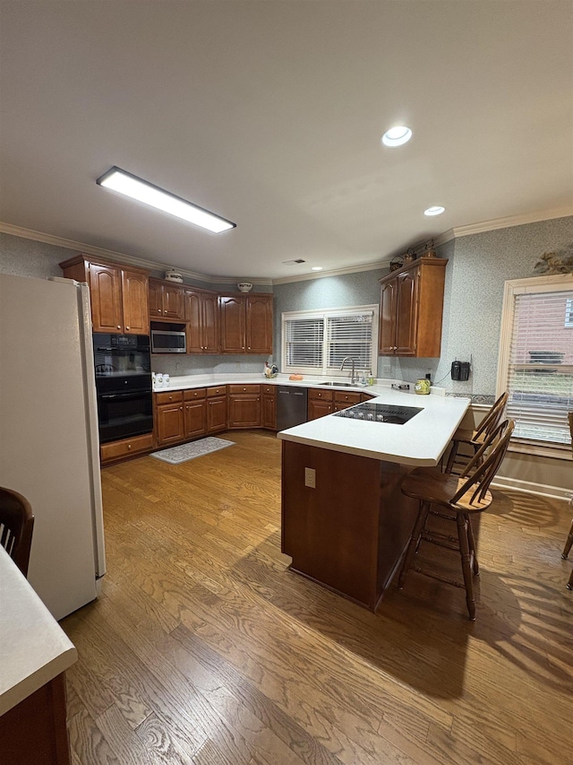 kitchen featuring kitchen peninsula, a breakfast bar, sink, black appliances, and hardwood / wood-style flooring