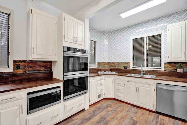 kitchen featuring backsplash, sink, light hardwood / wood-style flooring, appliances with stainless steel finishes, and white cabinetry