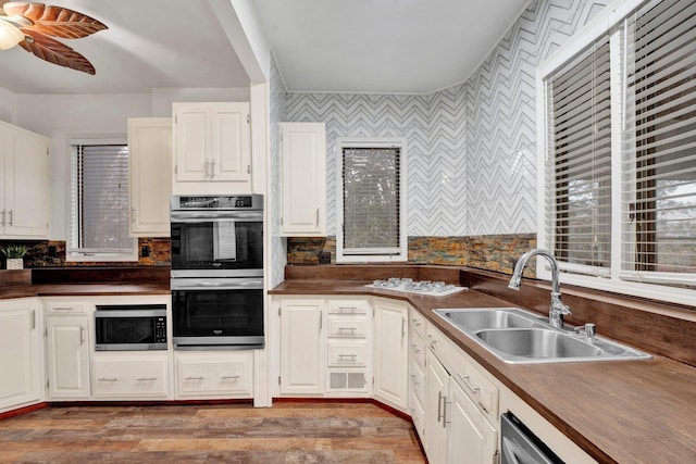 kitchen with light wood-type flooring, stainless steel appliances, ceiling fan, sink, and white cabinetry