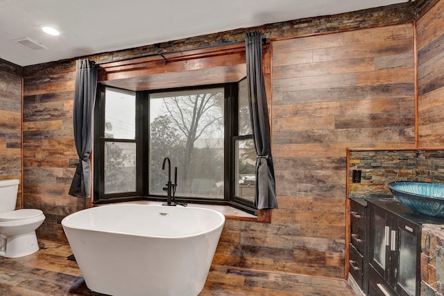 bathroom with hardwood / wood-style floors, toilet, a bathtub, and wood walls