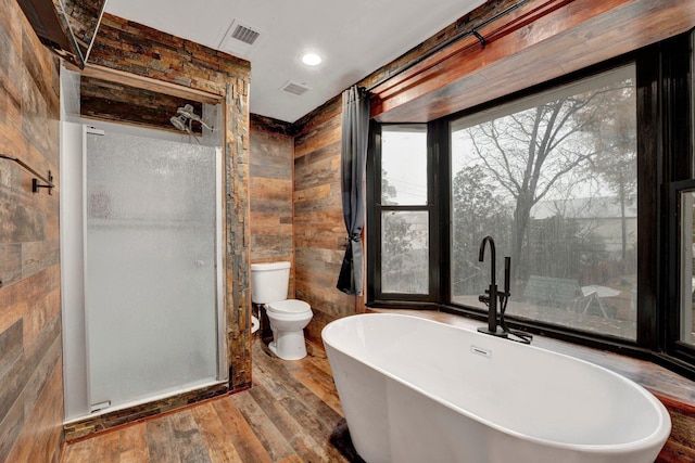 bathroom with a tub to relax in, hardwood / wood-style flooring, toilet, and wood walls