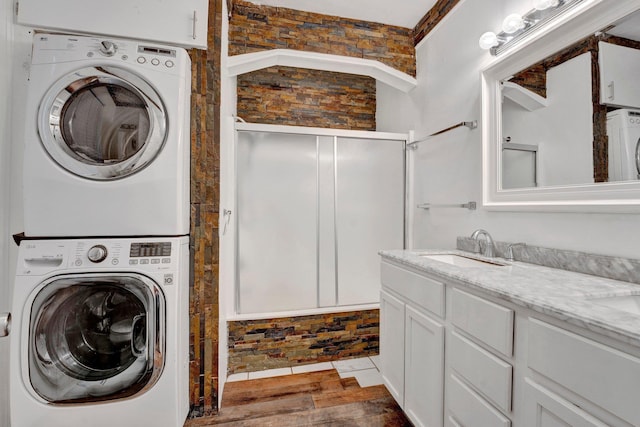 laundry room with hardwood / wood-style floors, stacked washing maching and dryer, and sink