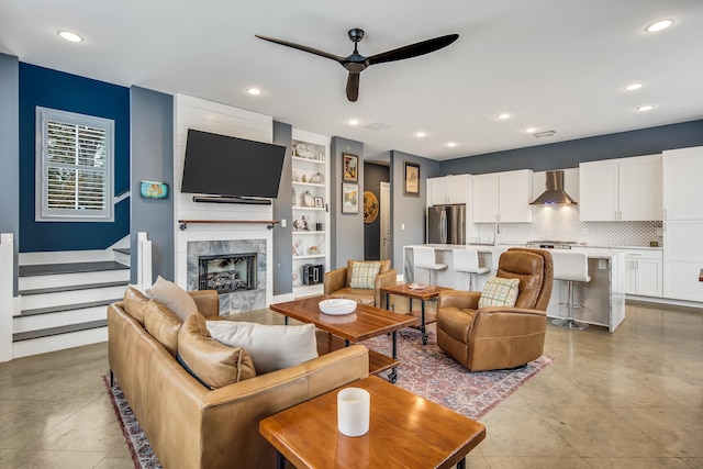 living room featuring a tile fireplace, built in features, and ceiling fan