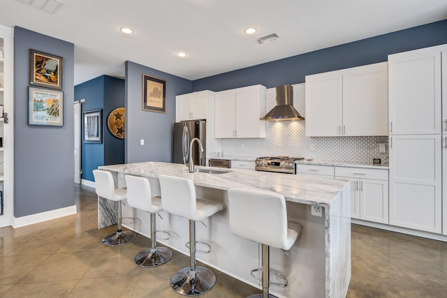 kitchen featuring a breakfast bar, appliances with stainless steel finishes, white cabinets, a center island with sink, and wall chimney exhaust hood