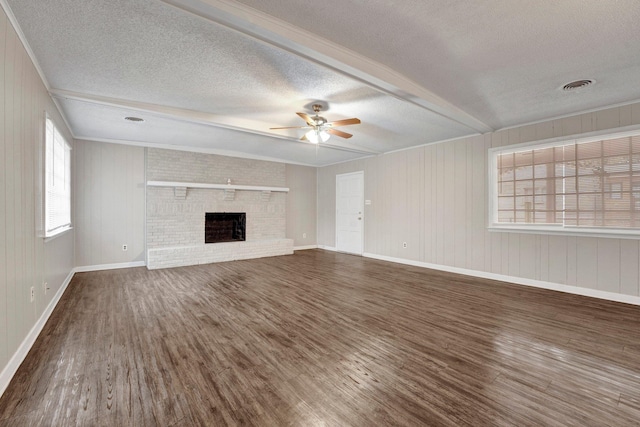 unfurnished living room with wood walls, a brick fireplace, ceiling fan, a textured ceiling, and dark hardwood / wood-style flooring