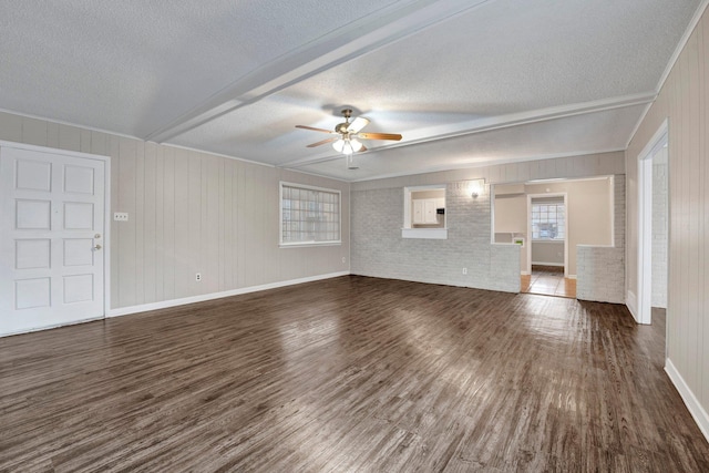 unfurnished living room with ceiling fan, dark wood-type flooring, crown molding, wood walls, and a textured ceiling