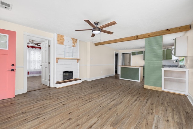 unfurnished living room featuring a large fireplace, ceiling fan, beam ceiling, and wood-type flooring