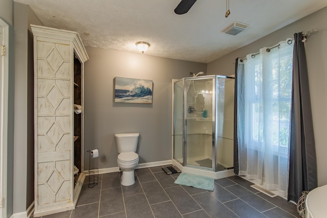 bathroom featuring tile patterned floors, ceiling fan, toilet, a textured ceiling, and a shower with shower door