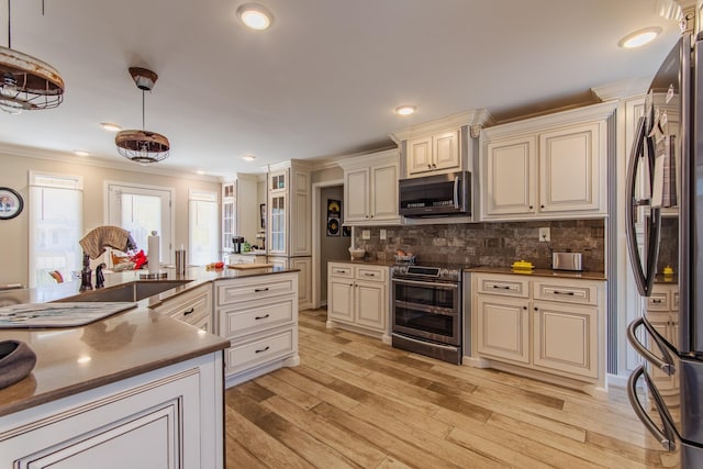 kitchen featuring pendant lighting, stainless steel appliances, light wood-type flooring, and cream cabinetry