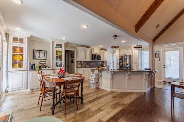 kitchen with stainless steel appliances, vaulted ceiling with beams, pendant lighting, light hardwood / wood-style floors, and a kitchen island with sink