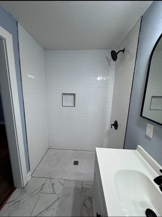 bathroom featuring a textured ceiling, vanity, and tiled shower