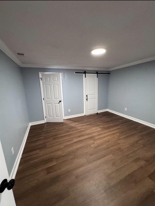 basement with a barn door, dark hardwood / wood-style floors, and ornamental molding