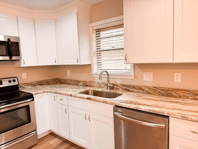 kitchen with light stone countertops, appliances with stainless steel finishes, light wood-type flooring, sink, and white cabinetry