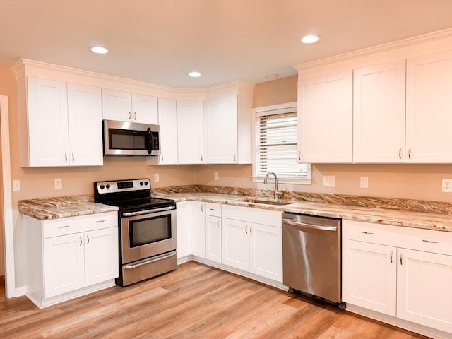 kitchen with sink, light stone countertops, light hardwood / wood-style floors, white cabinetry, and stainless steel appliances