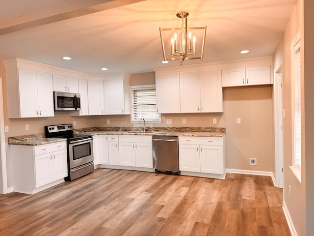 kitchen with white cabinets, hanging light fixtures, light wood-type flooring, light stone counters, and stainless steel appliances