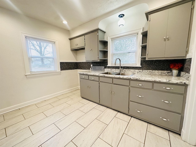 kitchen with a textured ceiling, backsplash, gray cabinets, and sink