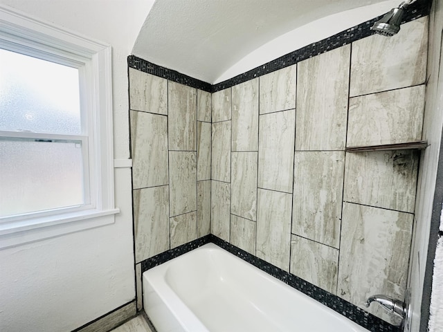 bathroom with a textured ceiling, tiled shower / bath combo, and lofted ceiling