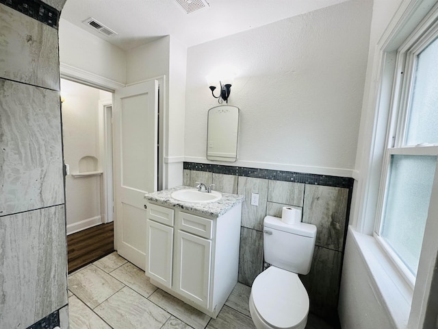 bathroom featuring vanity, toilet, and tile walls