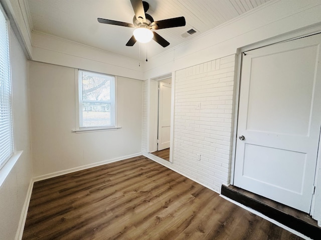 unfurnished bedroom featuring ceiling fan, dark hardwood / wood-style flooring, crown molding, and brick wall