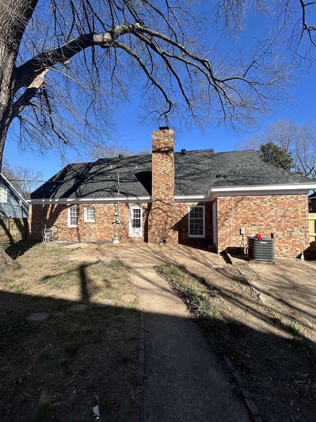 back of property with a chimney, central AC unit, and brick siding