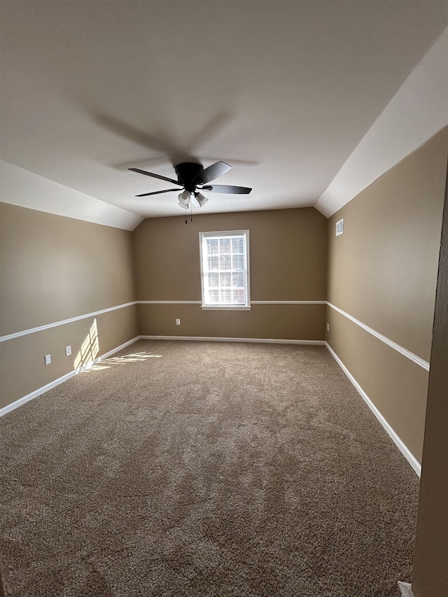 carpeted spare room featuring baseboards, vaulted ceiling, and a ceiling fan