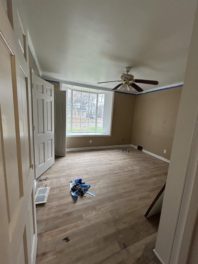 unfurnished bedroom with a ceiling fan, crown molding, baseboards, and wood finished floors