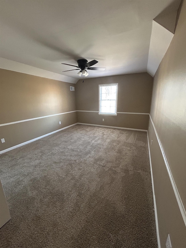 carpeted empty room featuring lofted ceiling, ceiling fan, visible vents, and baseboards