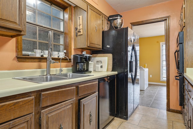 kitchen featuring sink, black dishwasher, a textured ceiling, light tile patterned flooring, and washer / clothes dryer