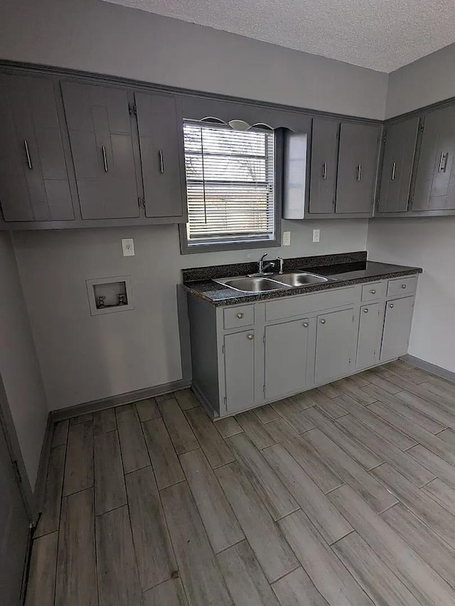 kitchen featuring a textured ceiling, light hardwood / wood-style flooring, gray cabinetry, and sink