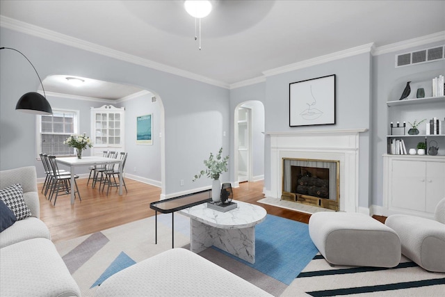 living room featuring light hardwood / wood-style floors, ceiling fan, crown molding, and a tiled fireplace